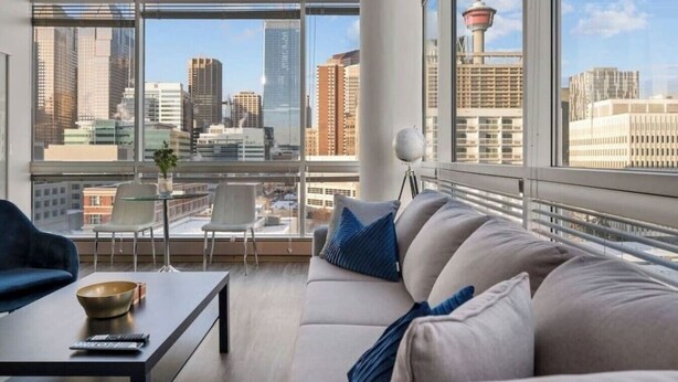 Un salon moderne avec vue sur la ville, comprenant un canapé, une table basse et un fauteuil.