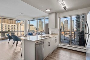 Een moderne keuken met een groot schiereiland, een eethoek met stoelen en grote ramen met uitzicht op de stad.