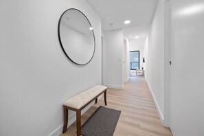 Un pasillo con un banco, un espejo redondo y una puerta que da a otra habitación.