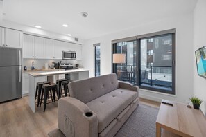 Un apartamento moderno con kitchenette, sofá gris, comedor y ventanas amplias que ofrecen una vista.