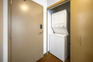 Uma lavanderia com máquina de lavar e secadora, uma porta com puxador e uma pequena tomada na parede.