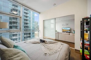 Quarto com uma cama grande, vista para a cidade, porta deslizante para uma sala de estar e uma estante de livros.