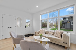 Un salon moderne comprenant un canapé, deux fauteuils, une table basse et une grande fenêtre donnant sur le quartier.