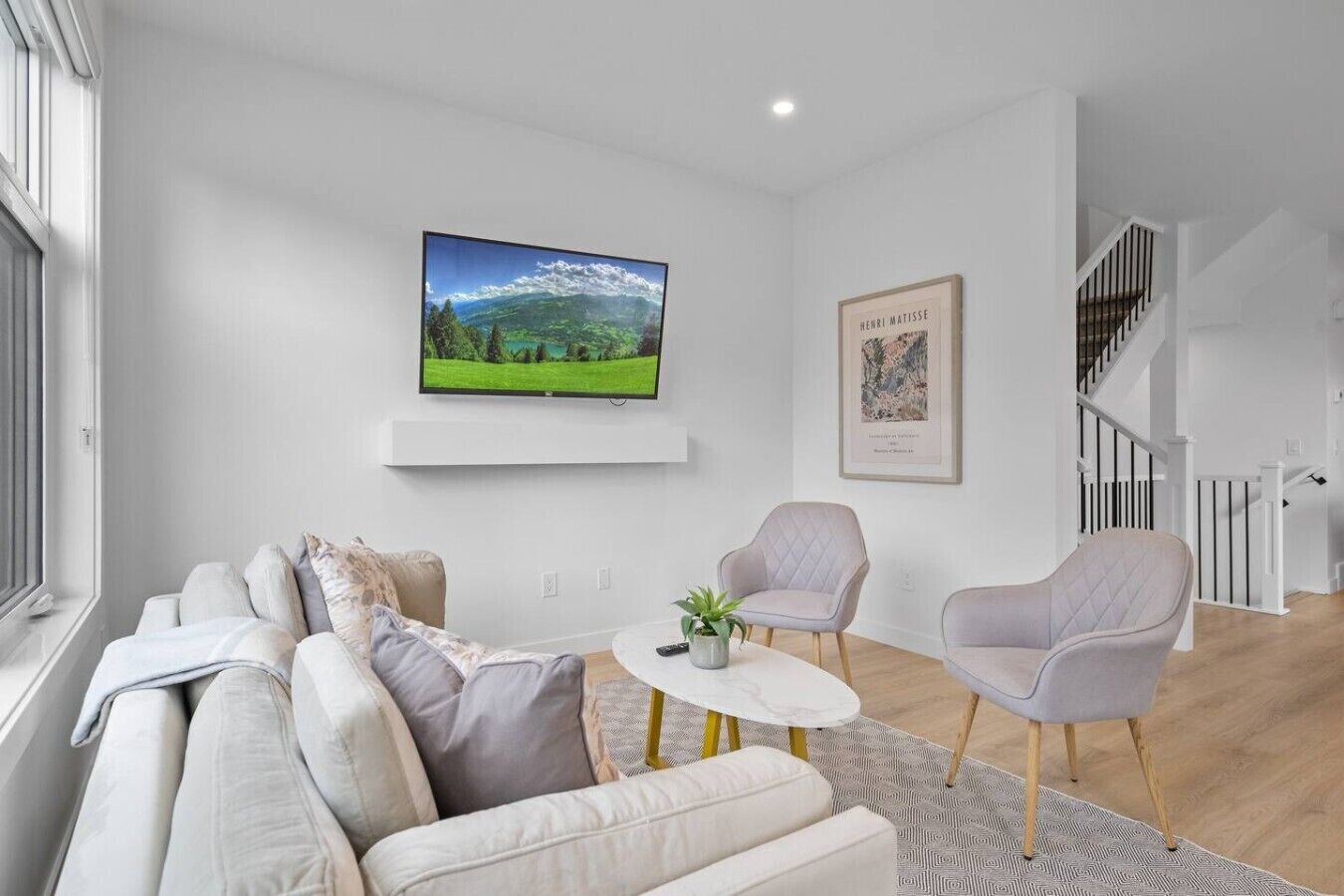 A modern living room with a sofa, two armchairs, a coffee table, a TV, and a staircase.