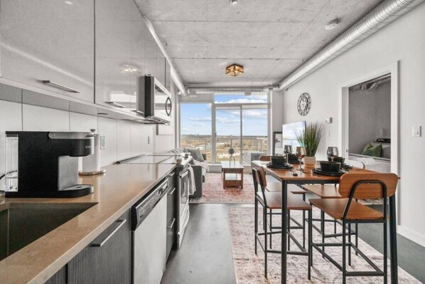 Una cocina moderna con cafetera, mesa de comedor, sillas y vistas por la ventana.