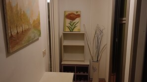 Een hal met een witte tafel, een landschapsprent, een plankje met een bloemschilderij en een decoratieve lamp.