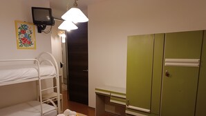 Een hotelkamer met stapelbedden, een bureau, een groene garderobe en een televisie aan de muur.