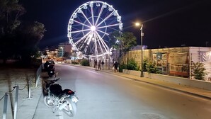 Een straat met een groot, verlichte reuzenrad op de achtergrond, een motorfiets aan de kant en een zebrapad.