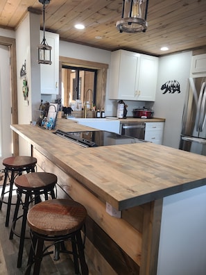 A modern kitchen with a wooden island, bar stools, stainless steel appliances, and a bear-themed wall decal.