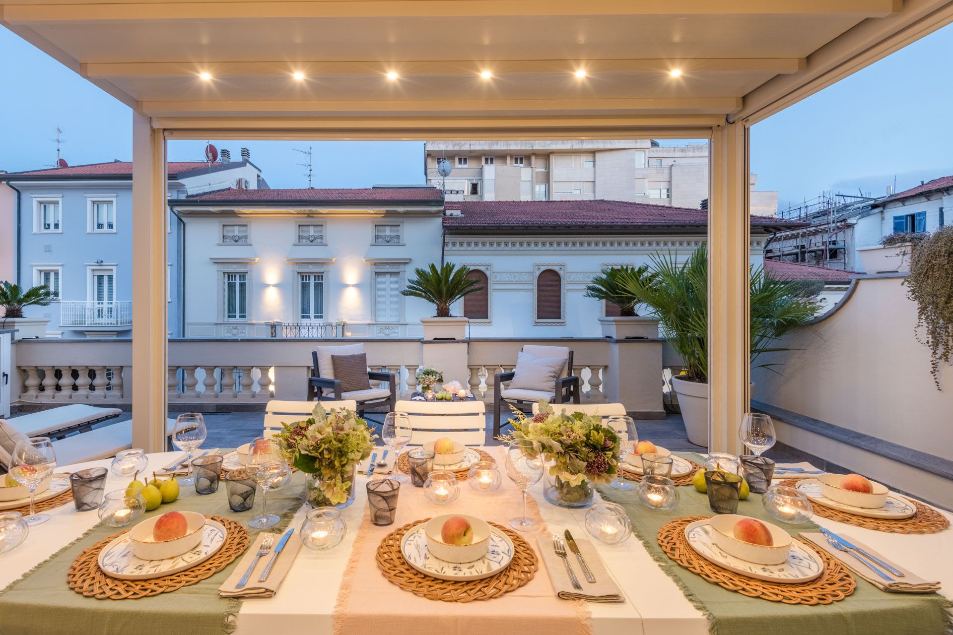 An outdoor dining area with a table set for four, surrounded by potted plants and candles.