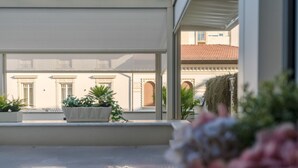 Un balcon orné de plantes en pot, d’où l’on peut admirer un immeuble aux fenêtres en arc de cercle.