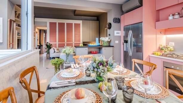 Une cuisine moderne avec des meubles roses, un réfrigérateur en acier inoxydable et un coin repas aménagé pour prendre un repas.
