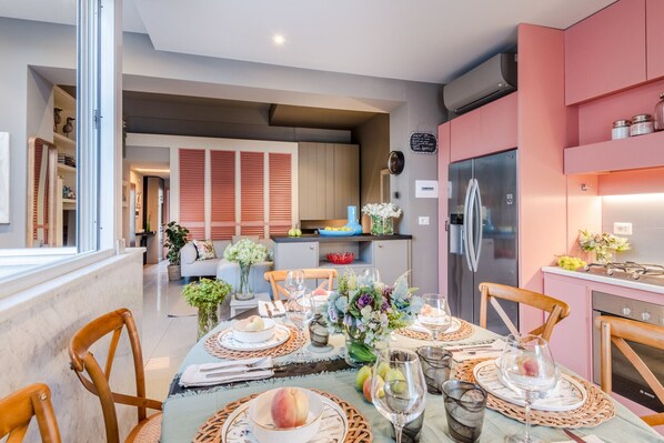 Une cuisine moderne avec des meubles roses, un réfrigérateur en acier inoxydable et un coin repas aménagé pour prendre un repas.