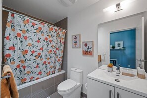 A bathroom with a toilet, a sink, a mirror, and a shower curtain with a fruit pattern.