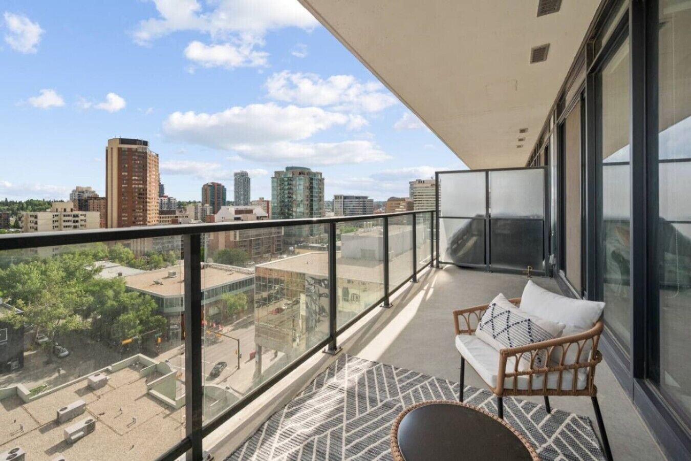 Un balcón con vista a la ciudad, una silla de mimbre y una alfombra estampada.