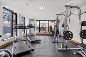 Une salle de sport équipée de tapis de course, de matériel de musculation et dotée d’une grande fenêtre donnant sur la ville.