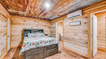 Une chambre dans un chalet en bois, avec un lit, une table de chevet, un climatiseur fixé au mur et une porte sur laquelle est apposée une pancarte.
