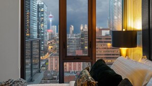 Une chambre dotée d’une grande fenêtre donnant sur la ville, d’un lit avec des oreillers et d’une lampe fixée au mur.