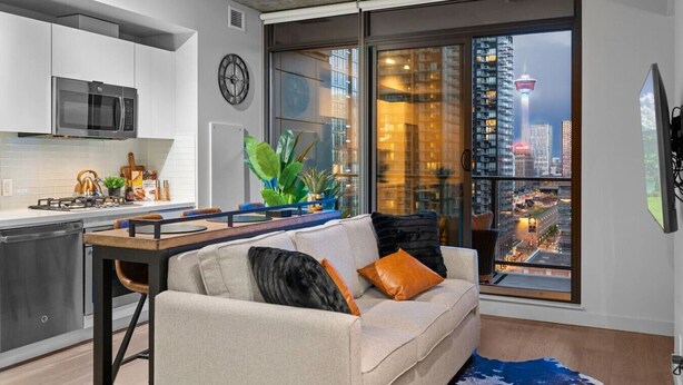 Un appartement moderne doté d’une cuisine, d’un canapé et d’une grande fenêtre offrant une vue sur la ville.