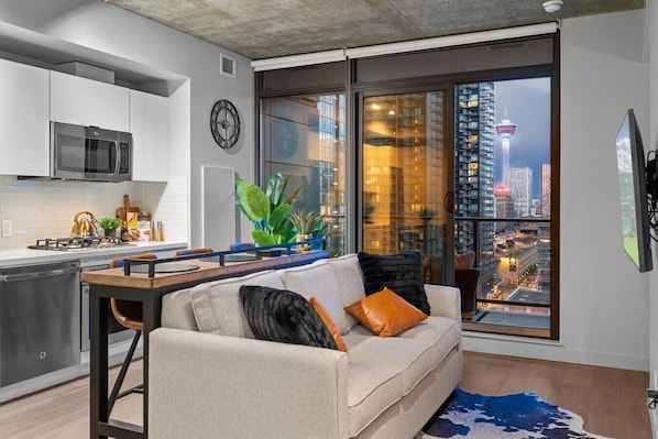 Un appartement moderne doté d’une cuisine, d’un canapé et d’une grande fenêtre offrant une vue sur la ville.