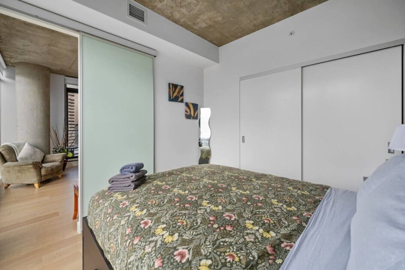 A bedroom with a floral bedspread, a sofa, a chair, and a wardrobe.