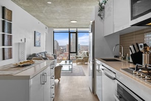 A modern kitchen with a city view, a dining area with a sofa and chairs, and a kitchen counter with utensils.
