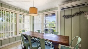 A dining area with a wooden table and green chairs, large windows with white blinds, and an air conditioning unit on the wall. - Dock * Water Views * Deck * Nature * Sunsets (Cedar Key)