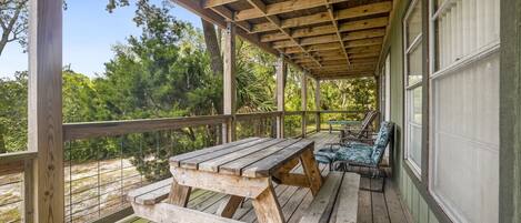 A wooden deck with a picnic table and chairs, surrounded by a wooden railing and large windows.