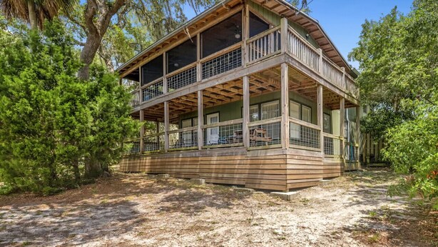 A two-story wooden cabin with a balcony, surrounded by trees. - Dock * Water Views * Deck * Nature * Sunsets (Cedar Key)
