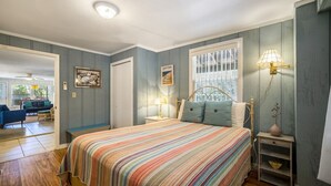 A bedroom with a striped bedspread, a nightstand with a lamp, a window with a view, and a door leading to another room. - Dock * Water Views * Deck * Nature * Sunsets (Cedar Key)
