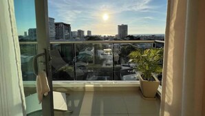 A balcony with a glass railing, a potted plant, and a view of the cityscape.