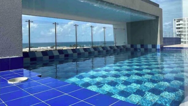A swimming pool with a view of the ocean, tiled in blue and white, and a modern building structure in the background.