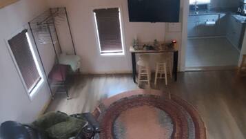 Une chambre mansardée avec un plafond en bois, un canapé en cuir noir, un tapis rond et un coin repas avec des tabourets.