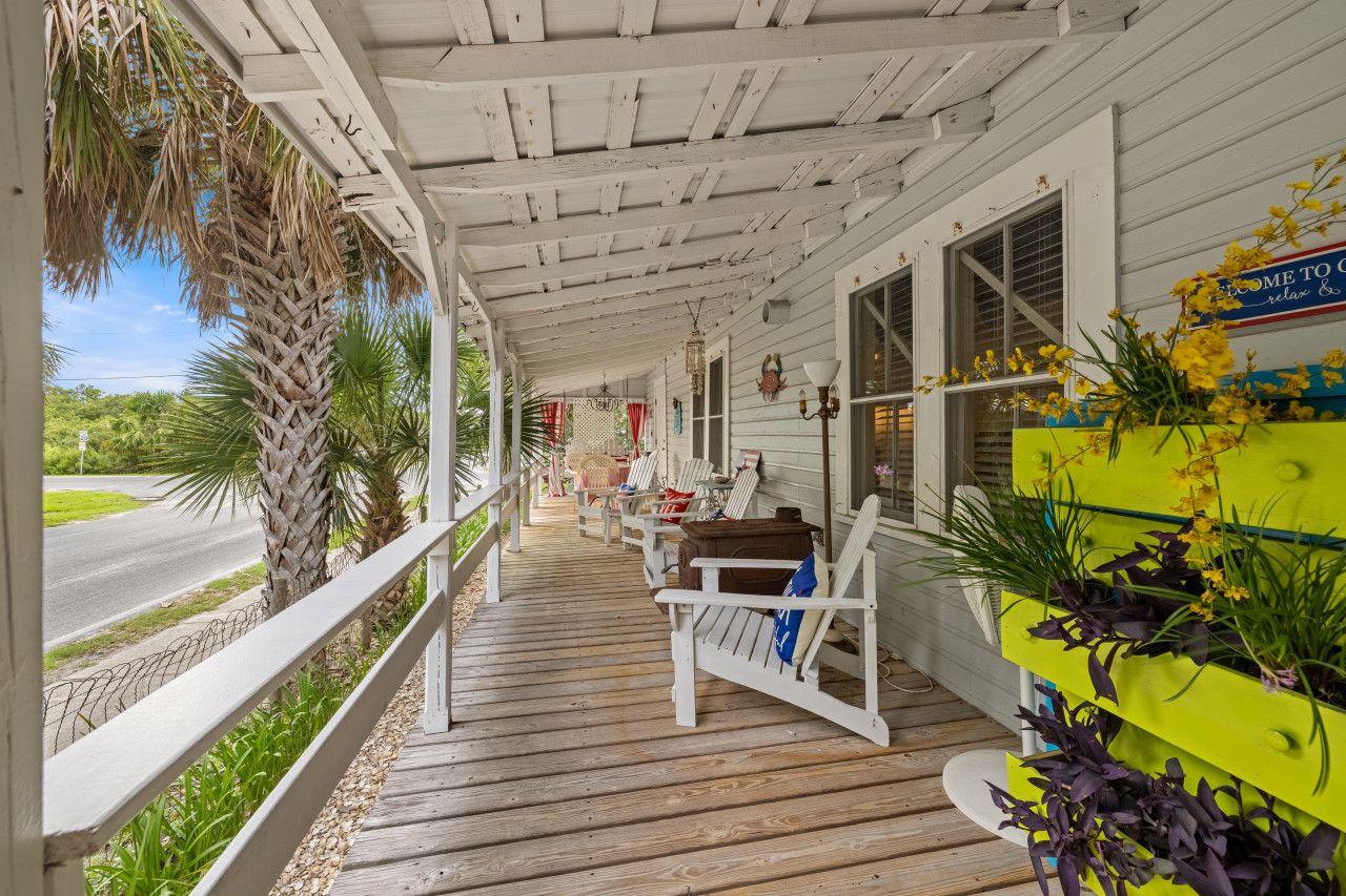 A covered porch with wooden railings, outdoor seating, and a view of the road.