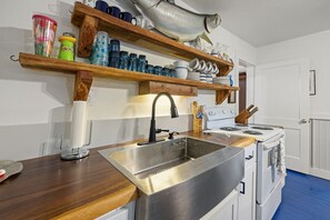 A kitchen with a stainless steel sink, wooden shelves, and a white stove. - Historic * Walkable * Downtown * Boat Parking * Fire Pit (Cedar Key)