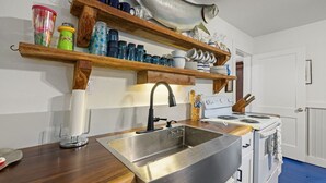 A kitchen with a stainless steel sink, wooden shelves, and a white stove.
