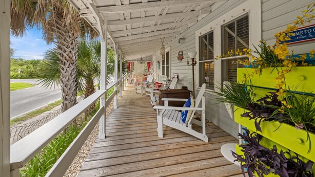 A covered porch with wooden railings, outdoor seating, and a view of the road.