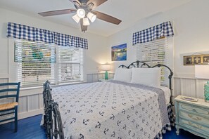 Un dormitorio con cama, una silla, un aparador y un ventilador de techo.