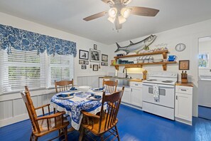Una cocina con una mesa de comedor preparada para cuatro personas, sillas de madera, una estufa blanca y un ventilador de techo.