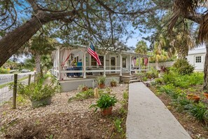 A rustic cabin with a porch, surrounded by potted plants and a pathway. - Historic * Walkable * Downtown * Boat Parking * Fire Pit (Cedar Key)