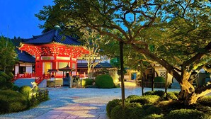 Un edificio tradicional japonés con fachada roja y blanca, rodeado de jardines cuidados y un sendero de piedra.