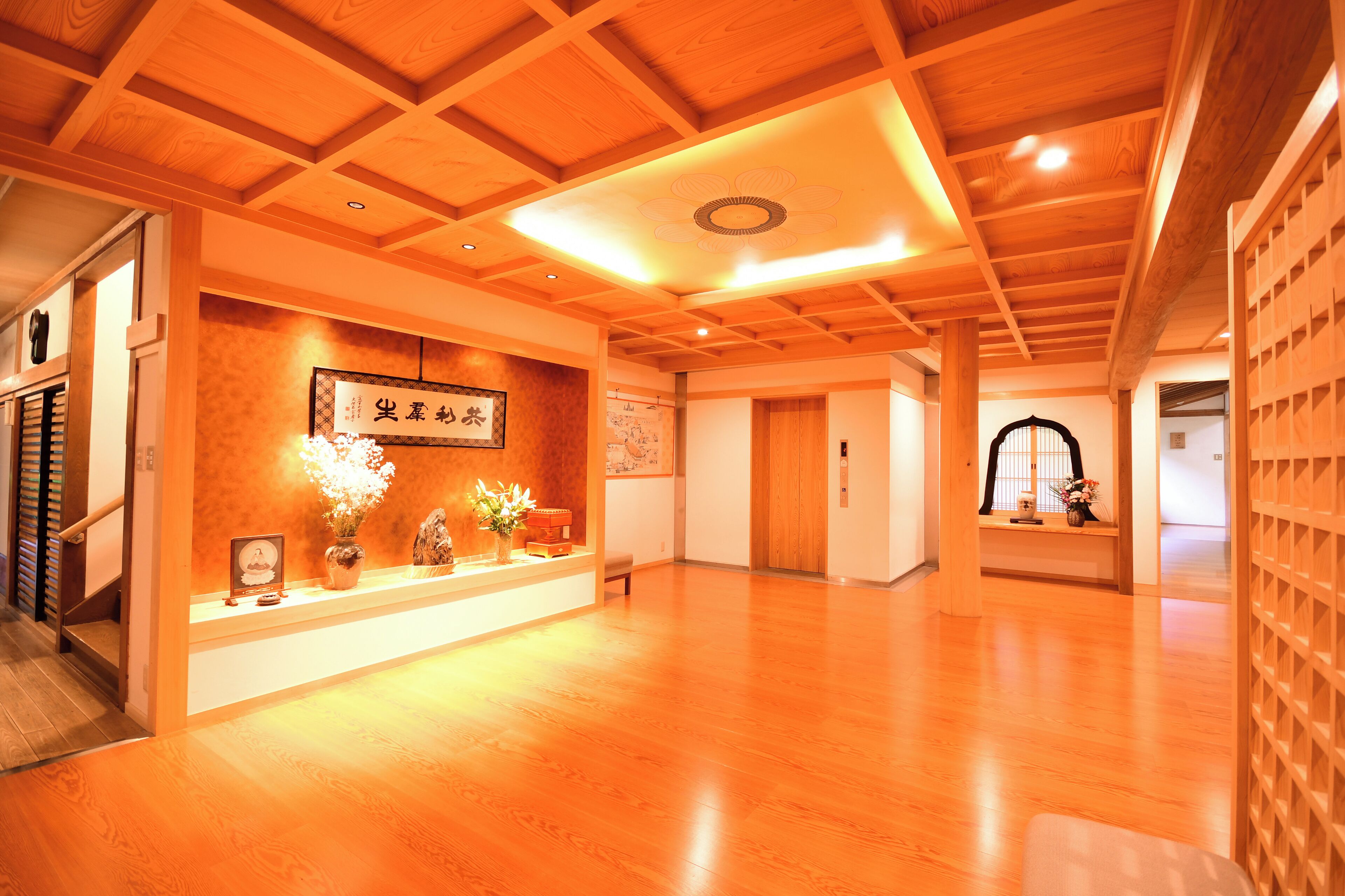 A spacious hallway with wooden flooring and ceiling, featuring a reception desk with a framed picture and potted plants.
