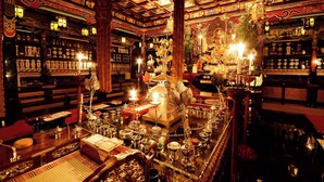Una habitación ornamentada con decoración tradicional, incluyendo un altar central con ofrendas, estantes con diversos objetos y un techo ricamente decorado.