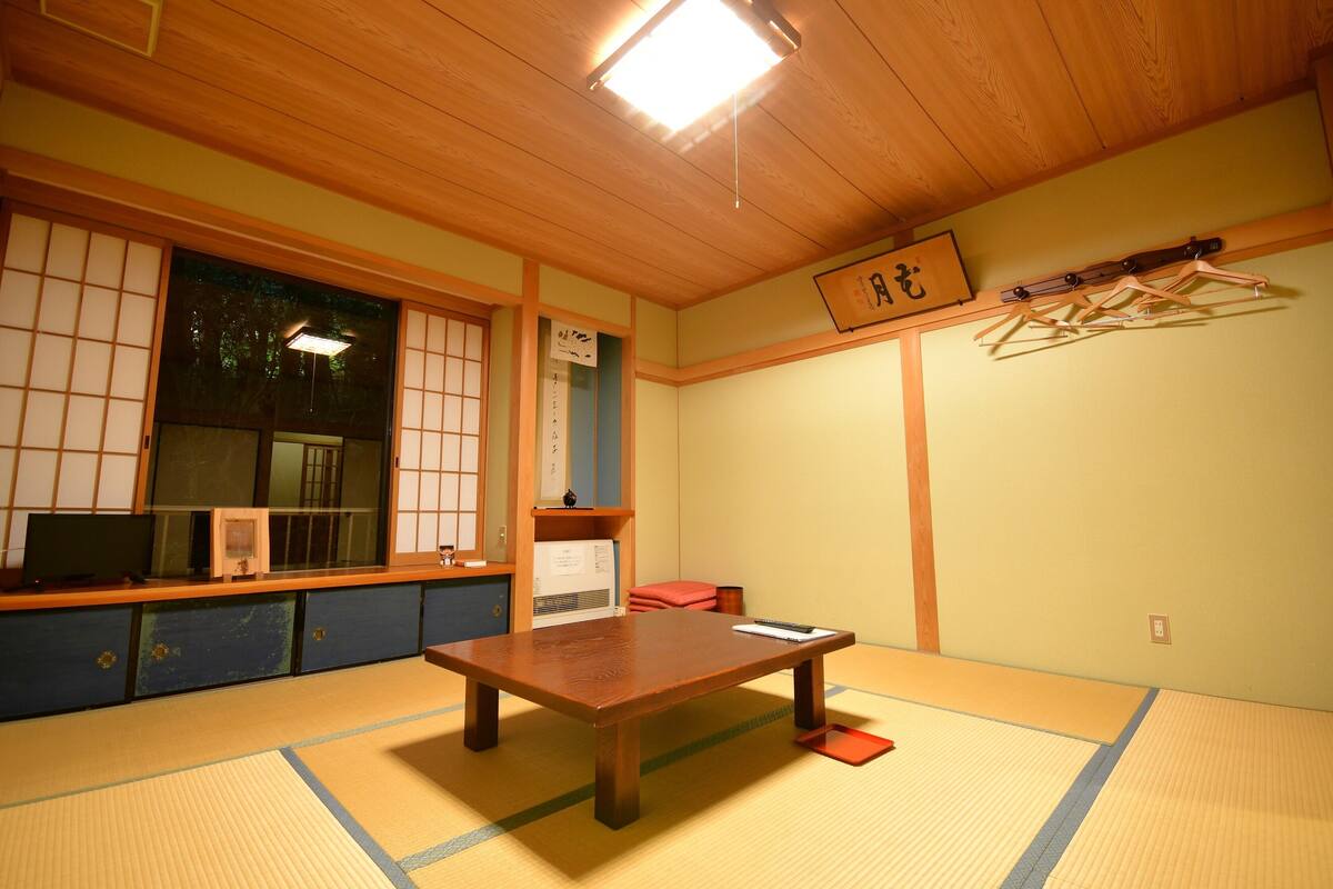 Een traditionele Japanse kamer met tatami vloerbedekking, een houten tafel, een shoji schuifwand en een kledingrek.