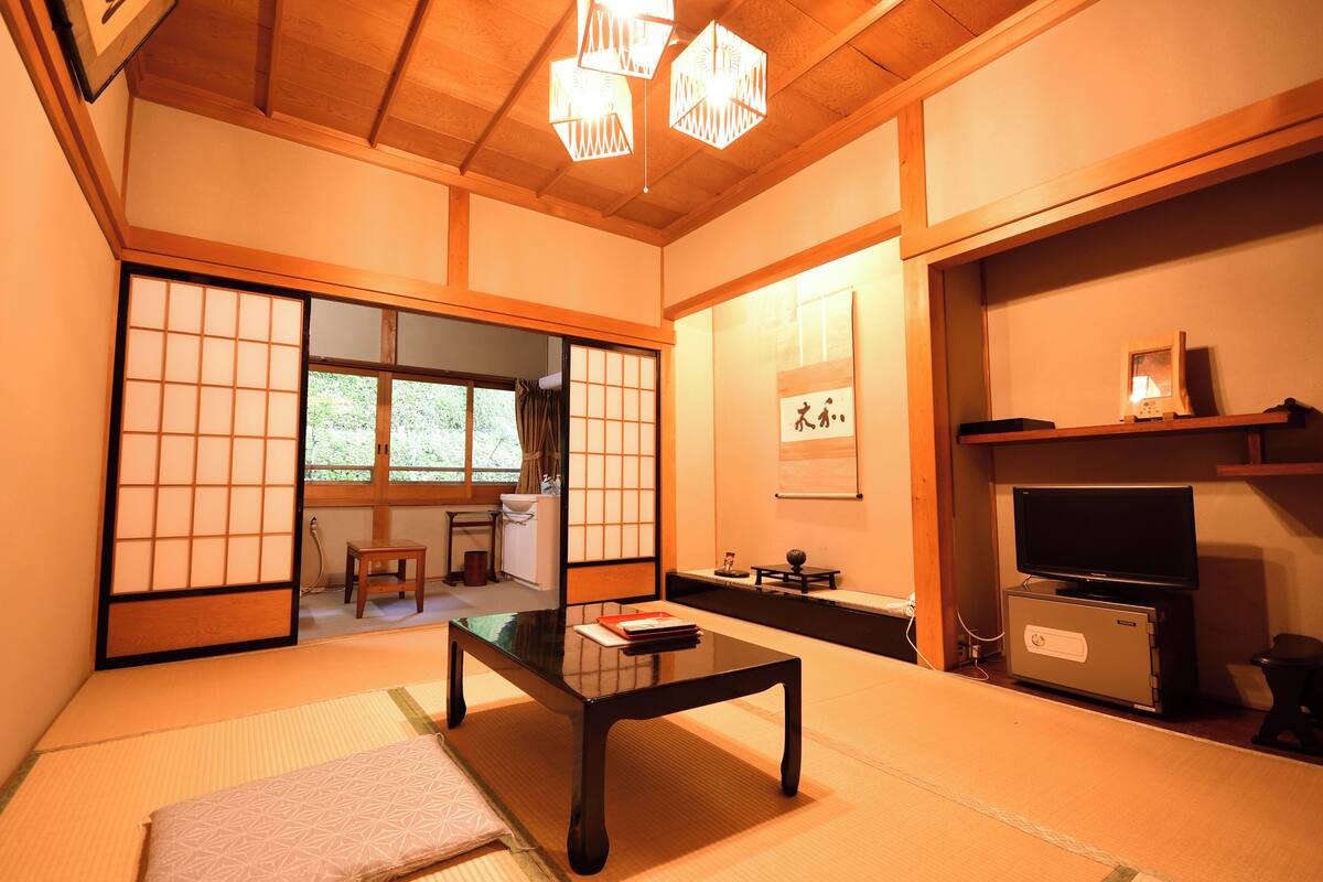 Een traditionele Japanse kamer met tatami vloeren, een lage tafel, een televisie en schuifdeuren naar een andere kamer.