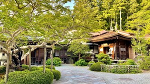 Un edificio tradicional japonés con fachada de madera, rodeado de abundante vegetación y un sendero de grava.