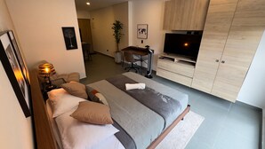 Un dormitorio moderno con una cama grande, un escritorio, un televisor y un armario.