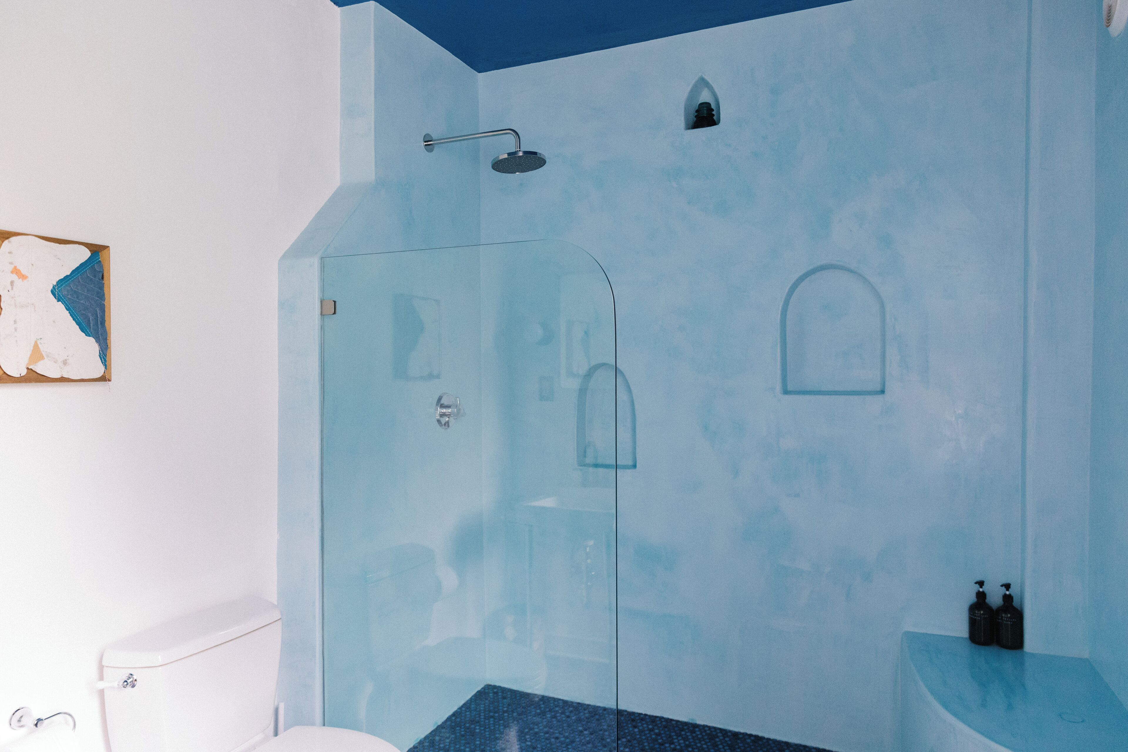 A bathroom with a glass shower enclosure, a white toilet, and a blue accent wall.