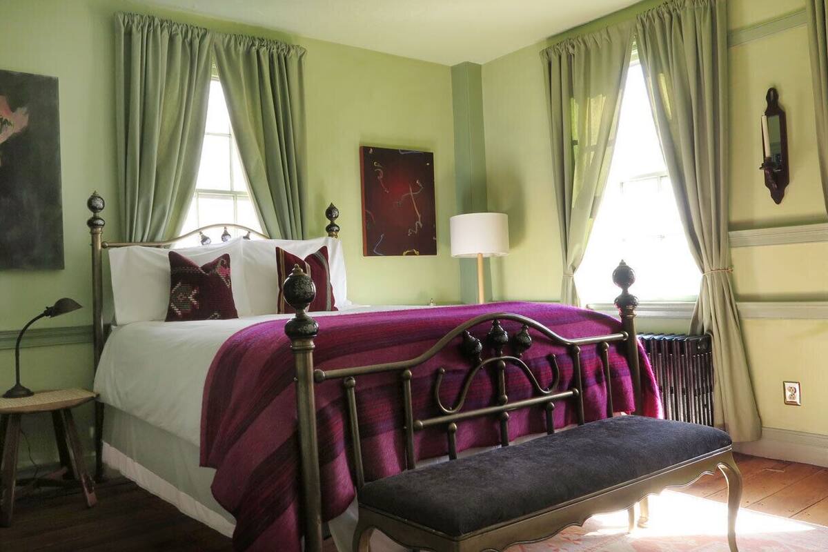 A bedroom with a bed, a bench, a chair, a lamp, and a painting on the wall.