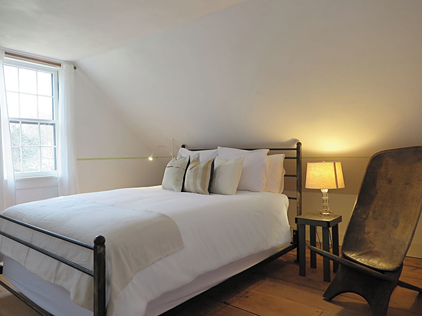 Une chambre à coucher avec un lit, une chaise, une table avec une lampe et une fenêtre.